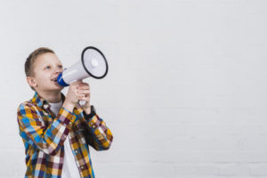 happy-boy-shouting-through-megaphone-standing-against-white-wall